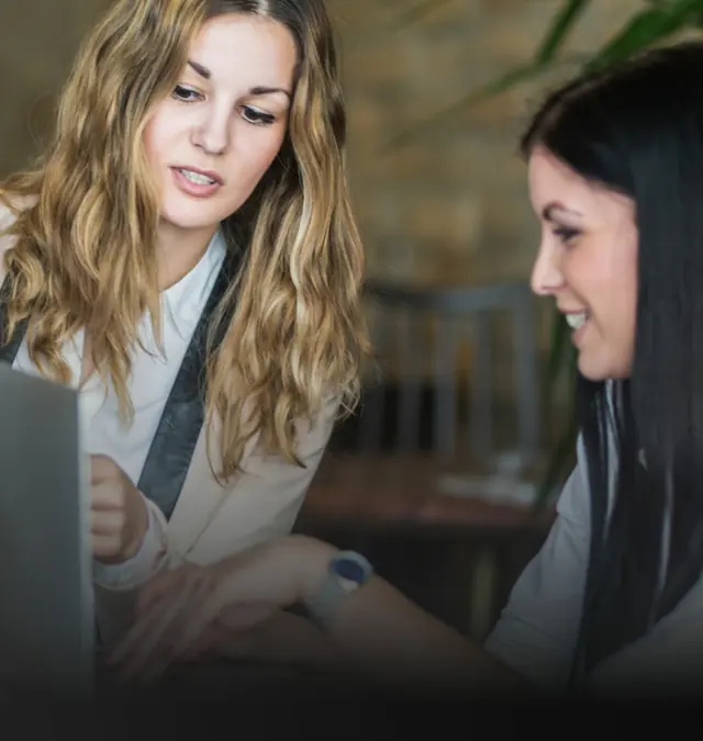Dos mujeres frente a una notebook: una le está explicando algo a la otra